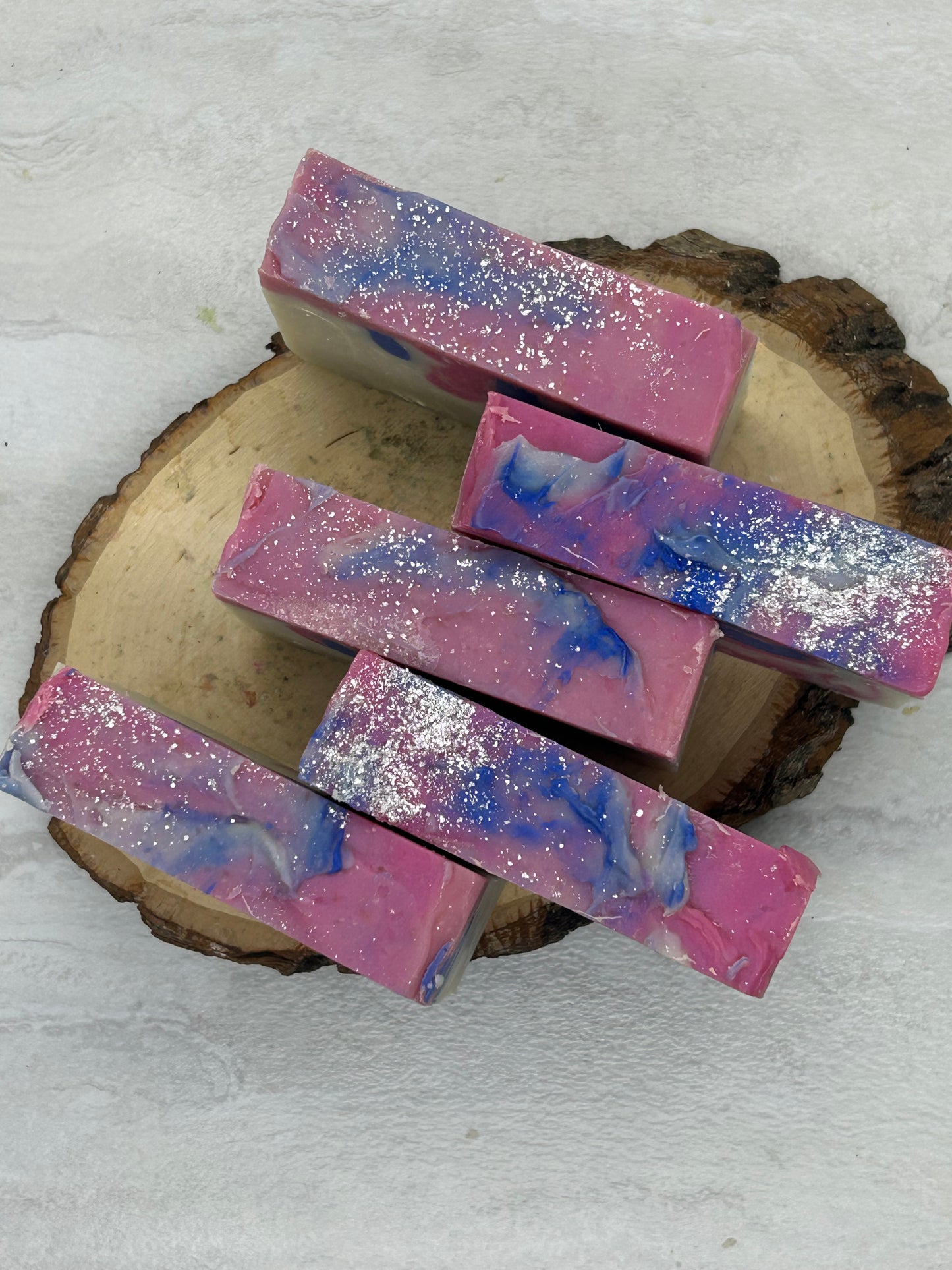 Colorful soap bars with glitter on a wooden block against a light background