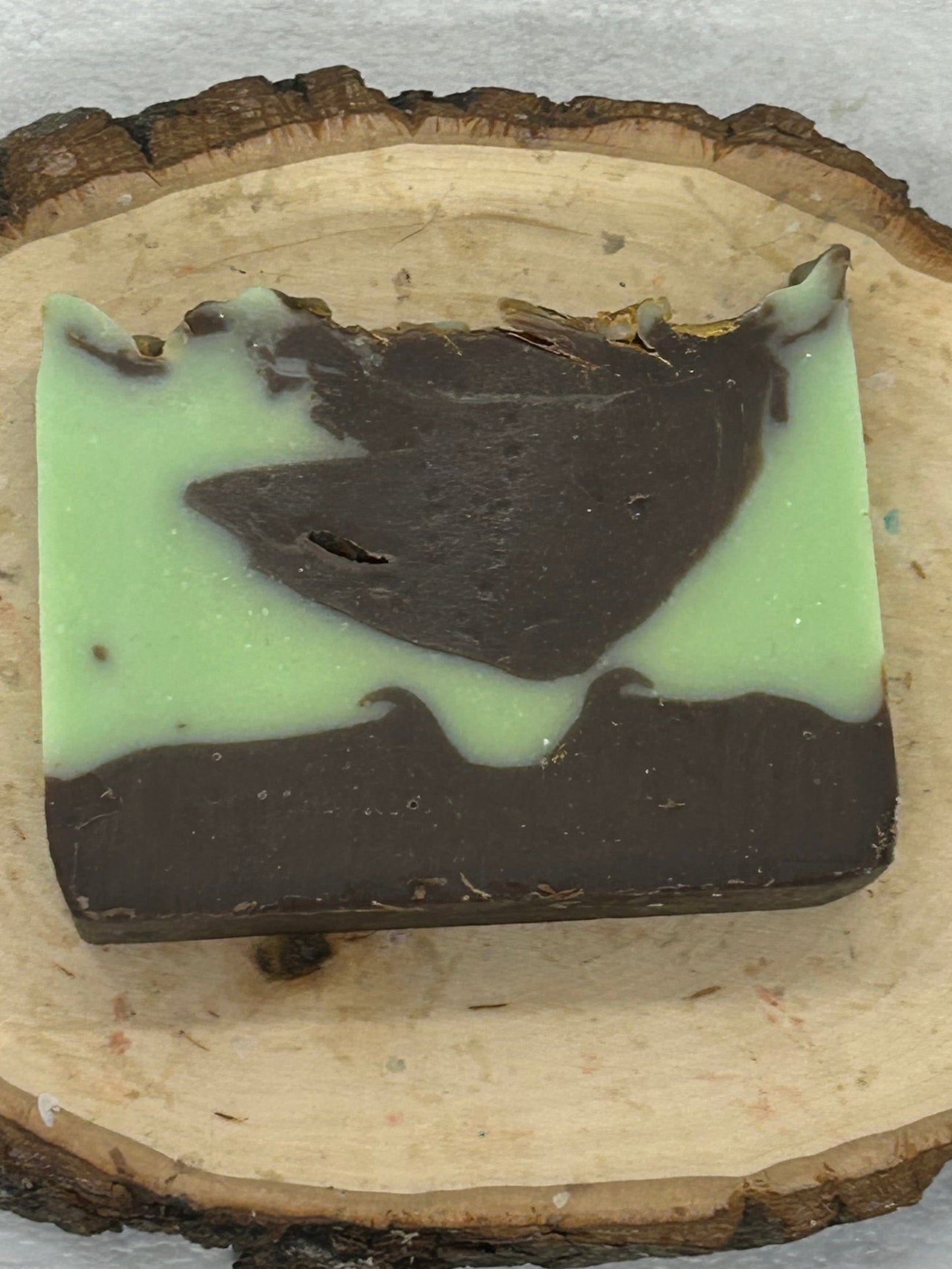 Mint and chocolate soap bar on a wooden slice with a white background