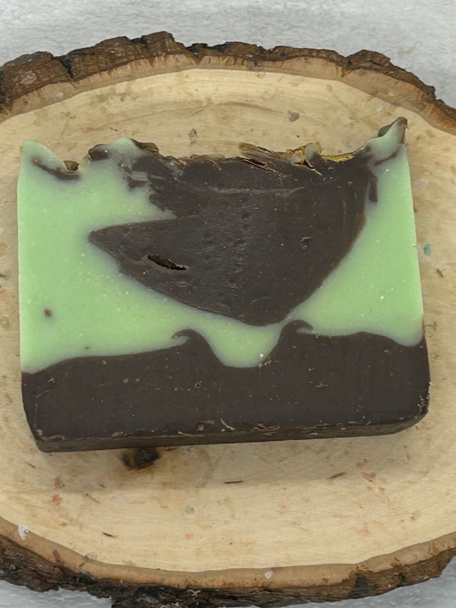 Mint and chocolate soap bar on a wooden slice with a white background
