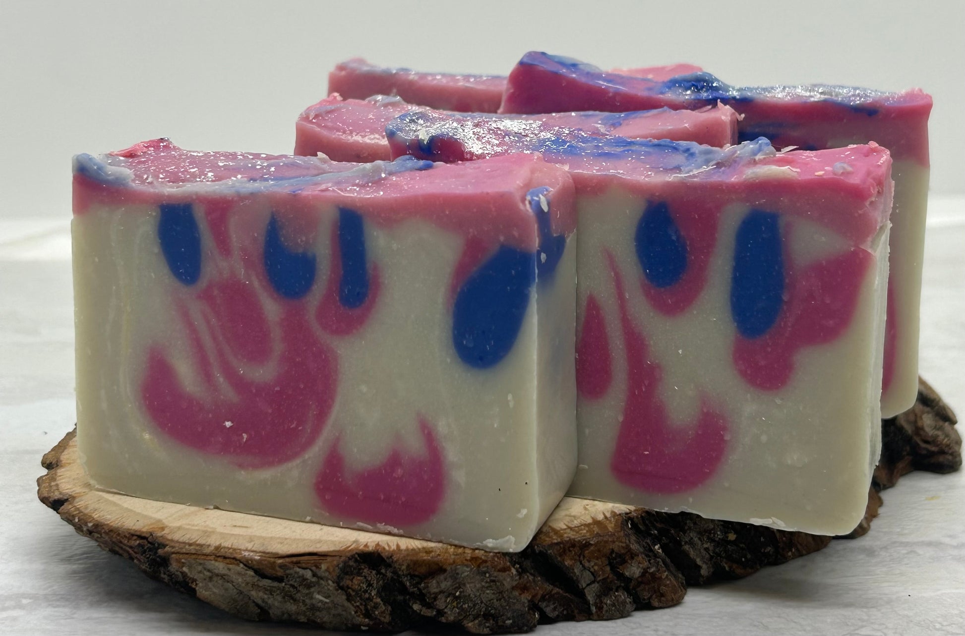 Three bars of soap with pink and blue swirls on a wooden block against a white background