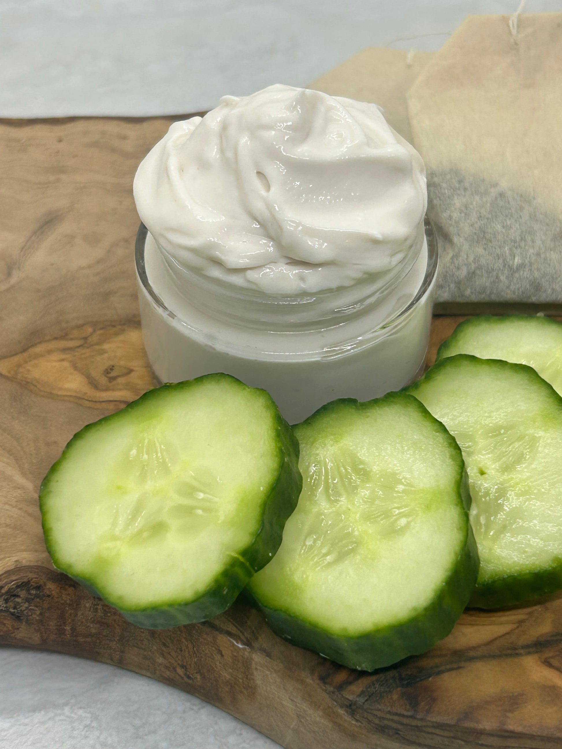 An open jar of cucumber & Green Tea eye with fresh cucumbers and tea bags on the side