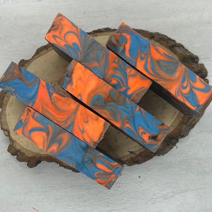 Five rectangular bars with a blue and orange marbled swirl pattern, arranged on a rustic round wood slice against a light gray textured background.
